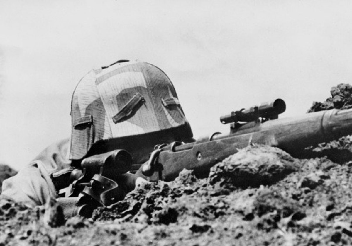 A German soldier in position with a ZF41 mounted rifle  with field glasses close at hand.